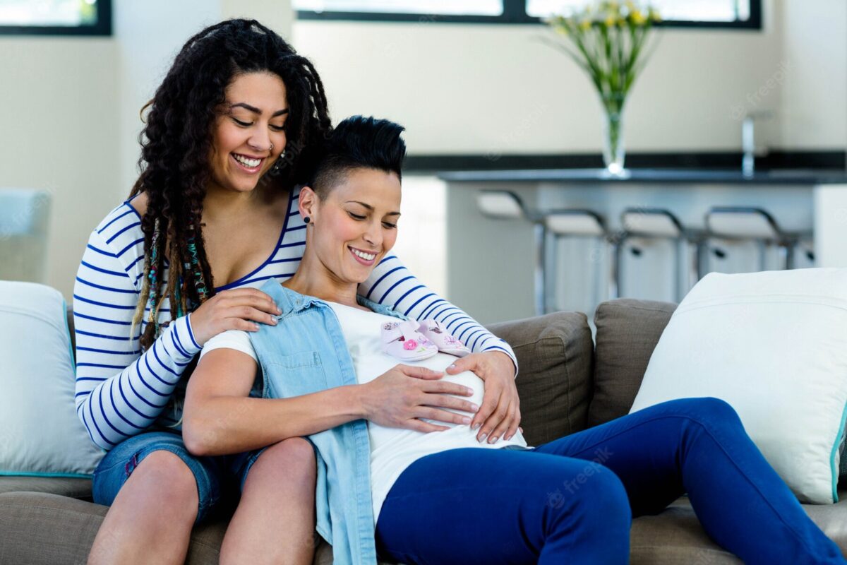 pareja-lesbianas-embarazadas-sentada-sofa-par-zapatos-bebe-rosa_107420-13364-1200x800.jpg